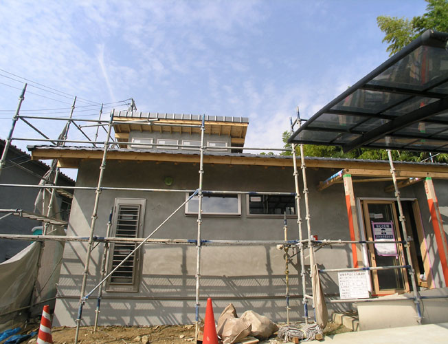 建物の正面から<br />現在、モルタル仕上が完了し養生中。仕上はハローコートという左官仕上で白色に仕上げます。杉のきれいな表情と白い塗り壁が美しい建築となると考えています。